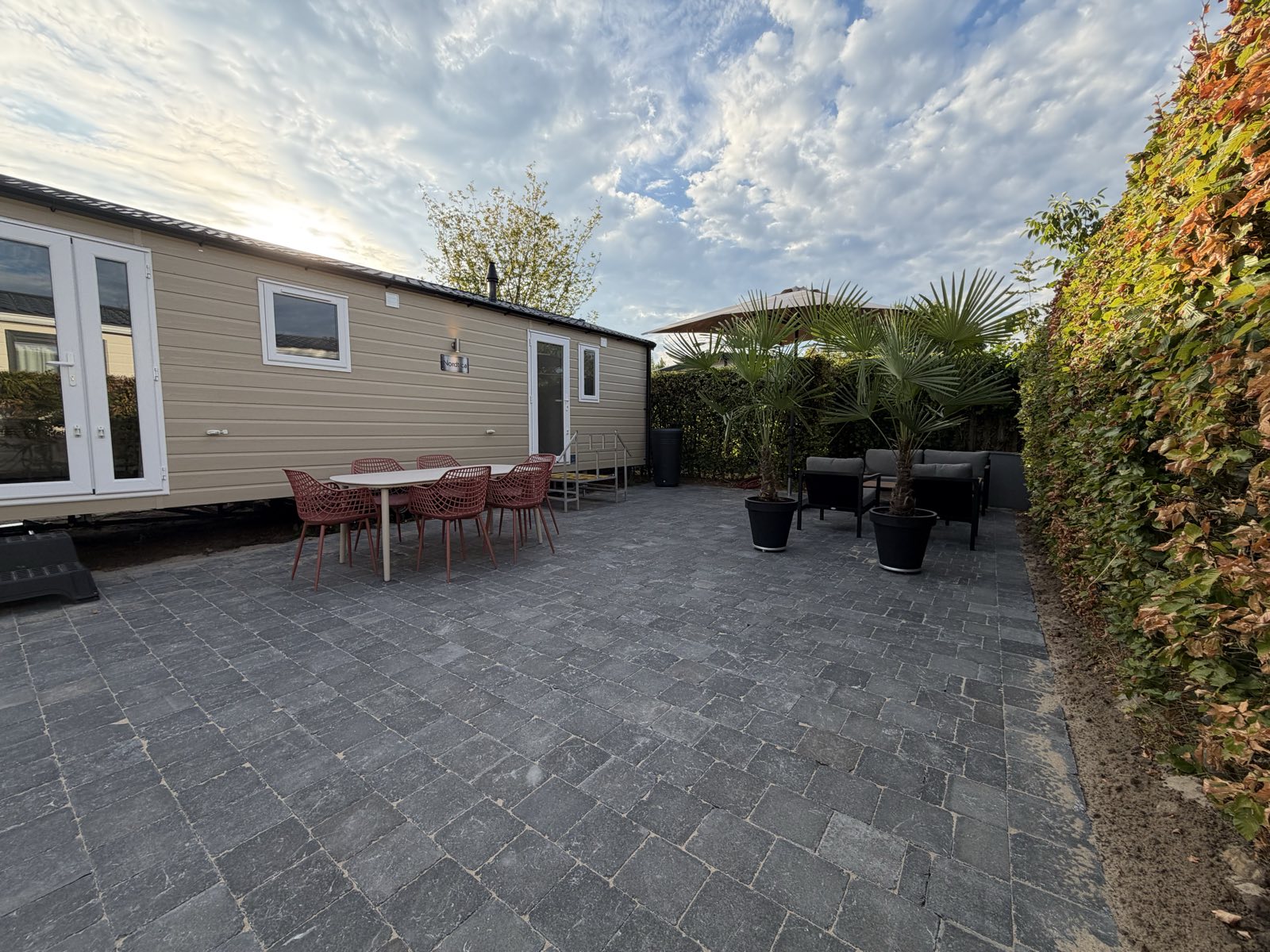 Het terras van Paardenweide 11 met eettafel, loungeset en parasol in de avondzon